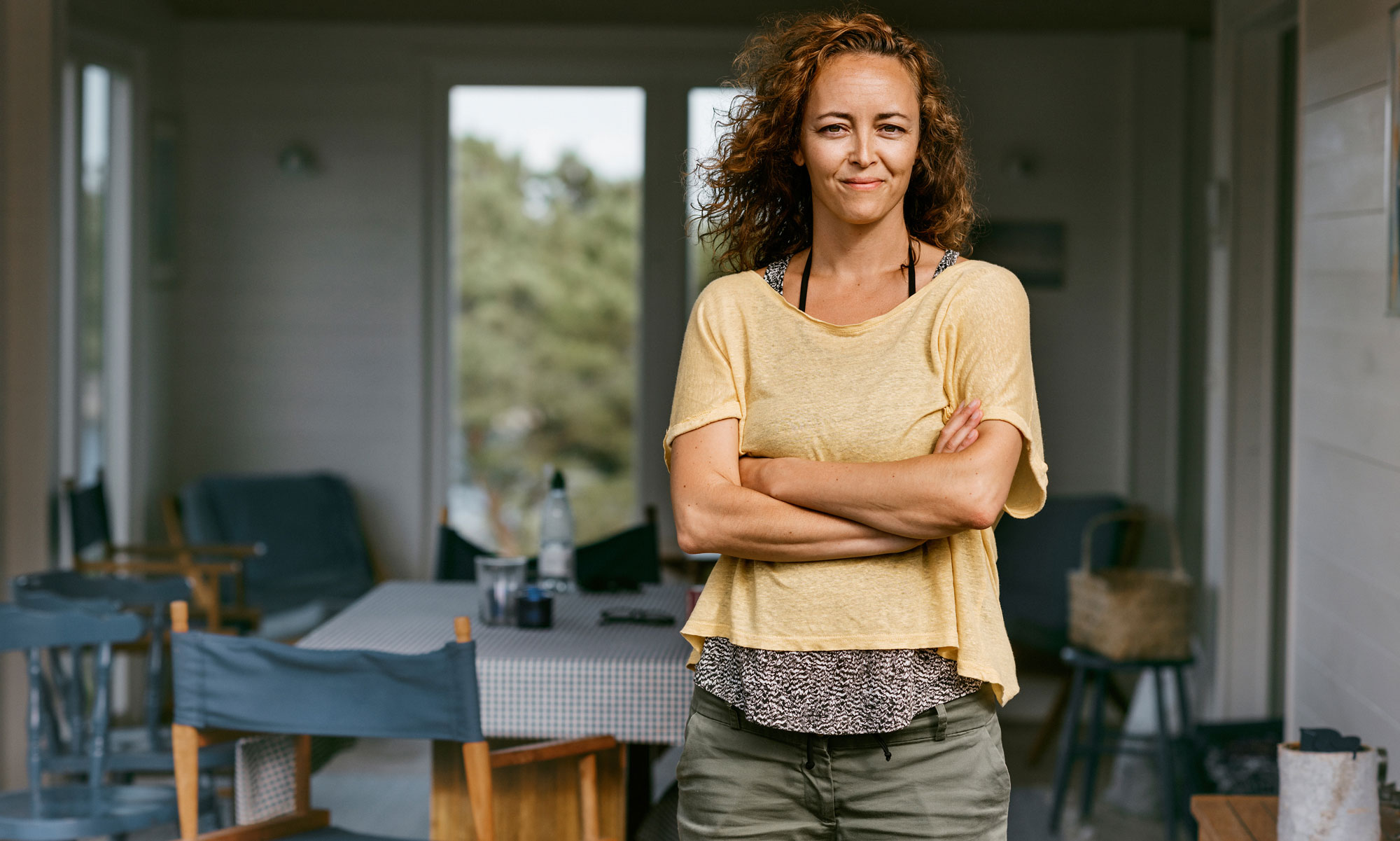 Kvinna med gul t-shirt och lockigt hår står i dörren till en sommarstuga