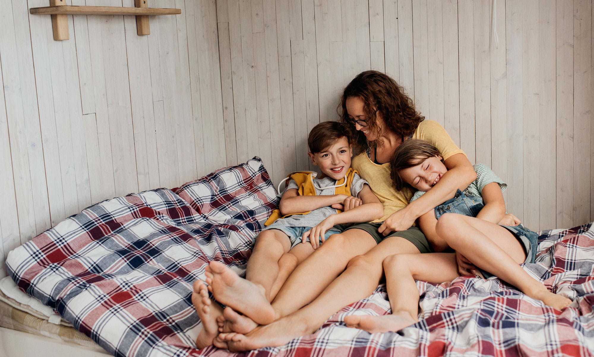 Mamma och två barn sitter på en säng och kramas